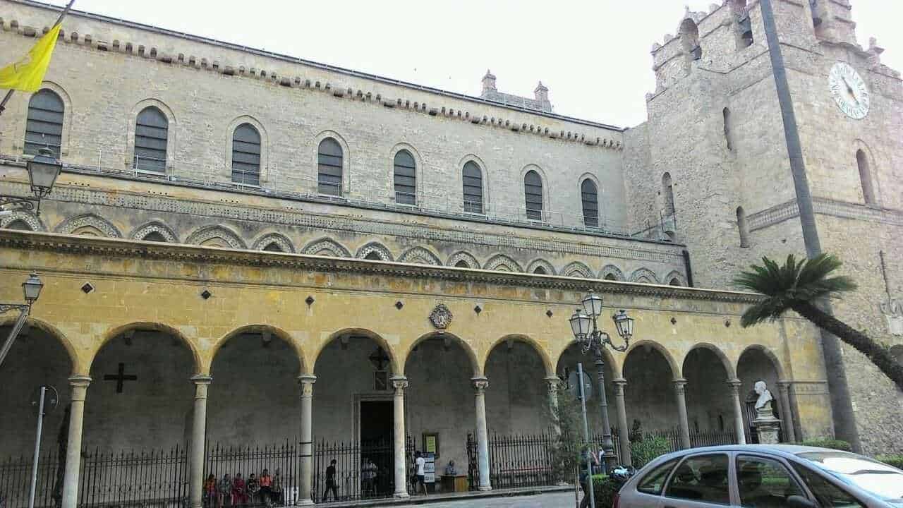 25 luoghi da visitare a Palermo e dintorni in stile arabo normanno 13 Antico edificio storico con portico e torre con orologio, situato in una suggestiva piazza italiana, con palme e lampioni, zona di grande interesse culturale e turistico, rappresenta un esempio di architettura medievale.