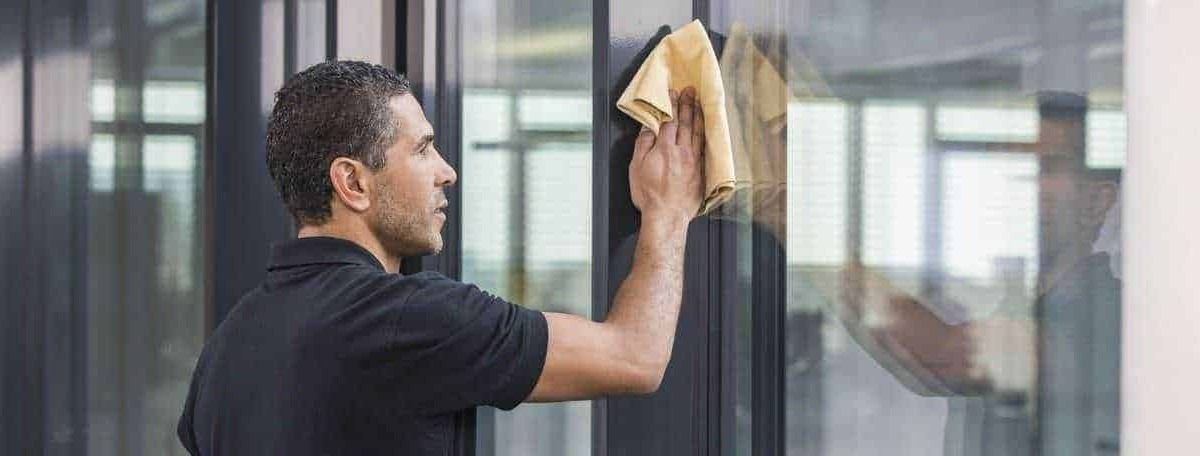 Pulizia vetrate professionale, uomo che utilizza panno in microfibra per detergere finestre in ufficio, servizio di cura e manutenzione vetri, ambiente di lavoro pulito e luminoso.