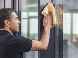 Pulizia vetrate professionale, uomo che utilizza panno in microfibra per detergere finestre in ufficio, servizio di cura e manutenzione vetri, ambiente di lavoro pulito e luminoso.