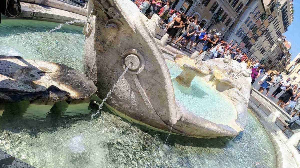 Fontana storica nel centro di Roma con persone che la ammirano e si rilassano, in un contesto urbano affollato, con edifici storici sullo sfondo.