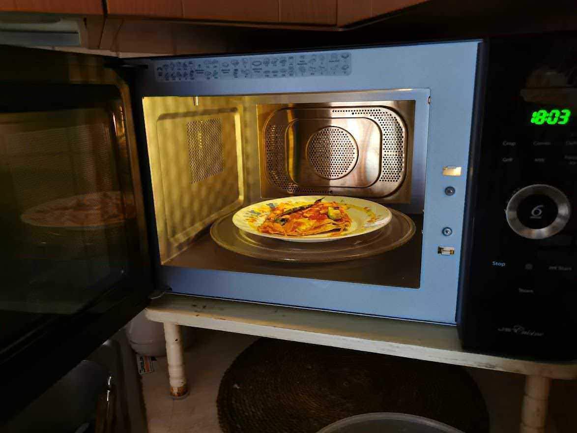 Piatto di pizza riscaldato nel microonde, cucina moderna, microonde acceso, cibo caldo, preparazione pasti, tecnologia da cucina, alimenti pronti, linea domestica, elettrodomestici moderni, cibo italiano, alimentazione salutare, cucina casalinga, ricette italiane, comfort culinario, attrezzature da cucina di alta qualità, apparecchiature per il riscaldamento, ambiente cucina accogliente, style di vita, alimenti pronti in modo rapido, innovazione culinaria.