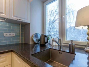 Finestra in cucina con vista sulla neve, lavello in acciaio inox, lampada decorativa e accessori da cucina come bollitore e dispenser di sapone, pareti in piastrelle blu.