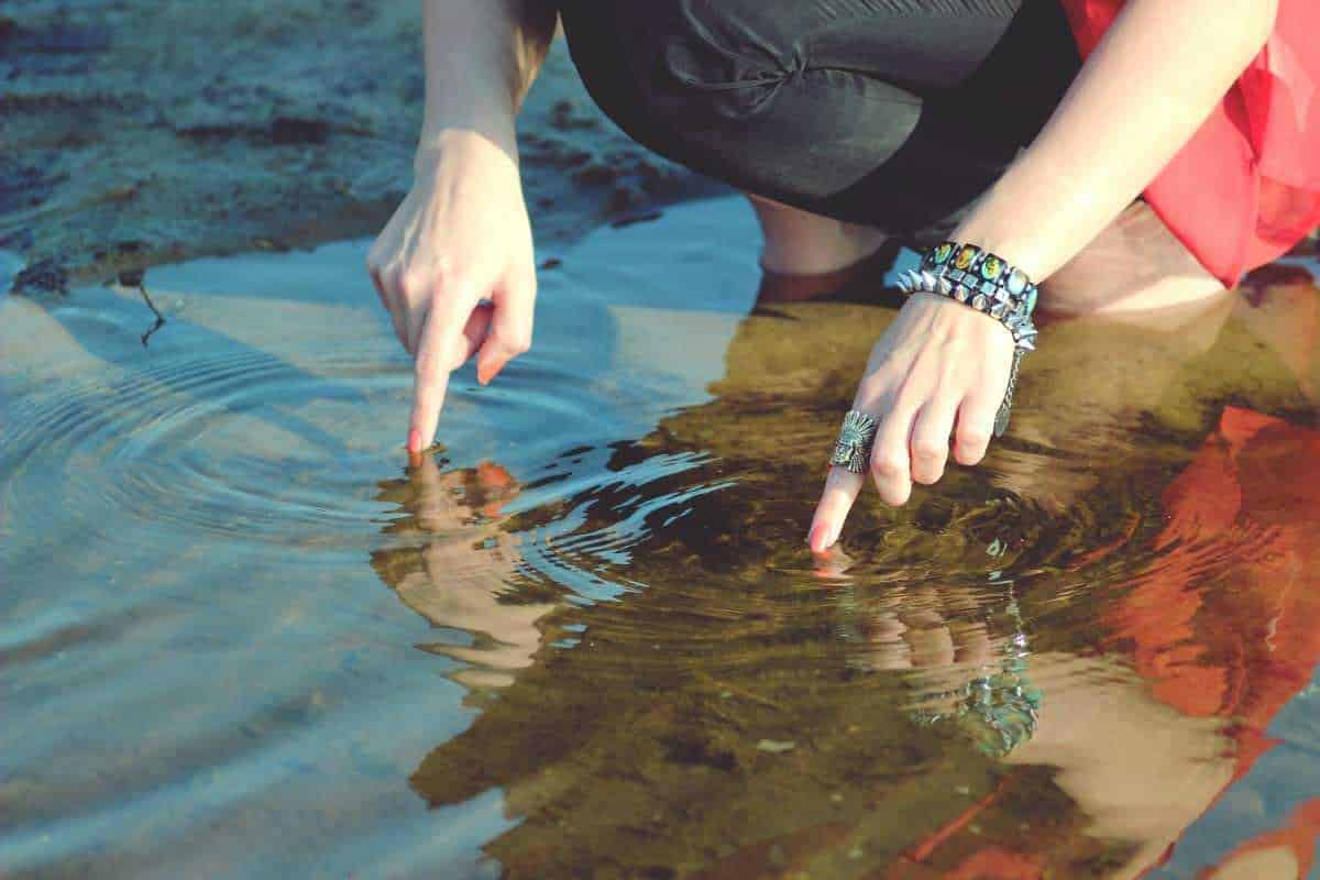Titolare Web. Foto di una persona che rovista nell'acqua di un ruscello con le dita. Scarpe da ginnastica e accessori decorative alla mano, ambiente naturale. Ideale per immagini di natura, avventura, esplorazione e outdoor.