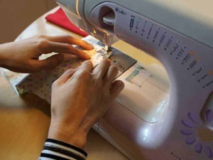 Macchina da cucire in funzione, mani che guidano il tessuto durante la cucitura, dettaglio di un’attività creativa e fai-da-te, ideale per articoli su artigianato e DIY.