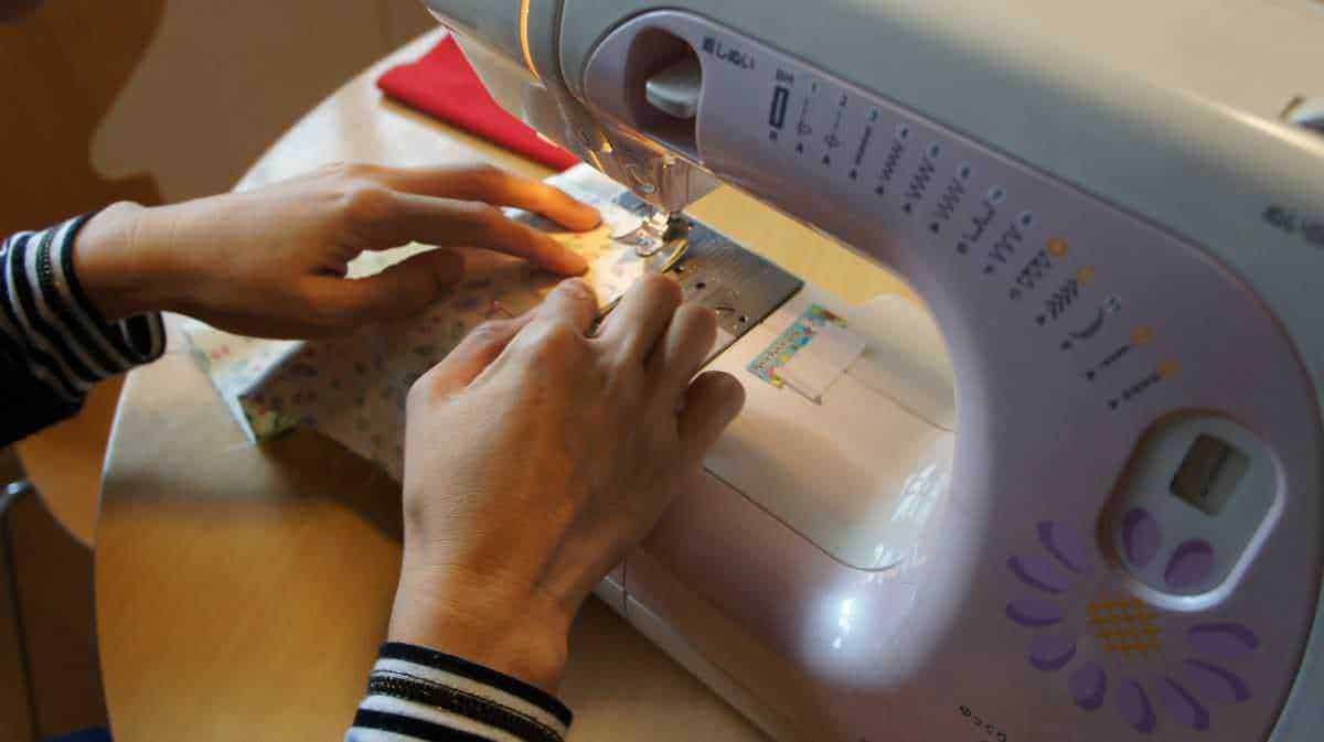 Macchina da cucire in funzione, mani che guidano il tessuto durante la cucitura, dettaglio di un’attività creativa e fai-da-te, ideale per articoli su artigianato e DIY.