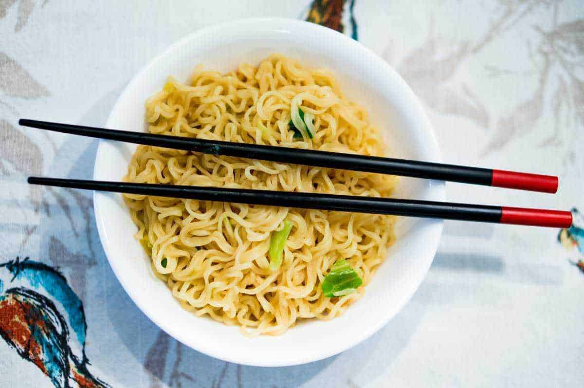 Deliziosi noodles istantanei in una ciotola bianca con bacchette nere e rosse, pronti per essere gustati, rappresentano la cultura culinaria asiatica.