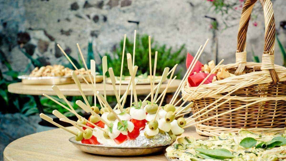 Finger food con spiedini di mozzarella, prosciutto e olive, perfetti per aperitivi estivi, con un'ambientazione rustica e naturale.