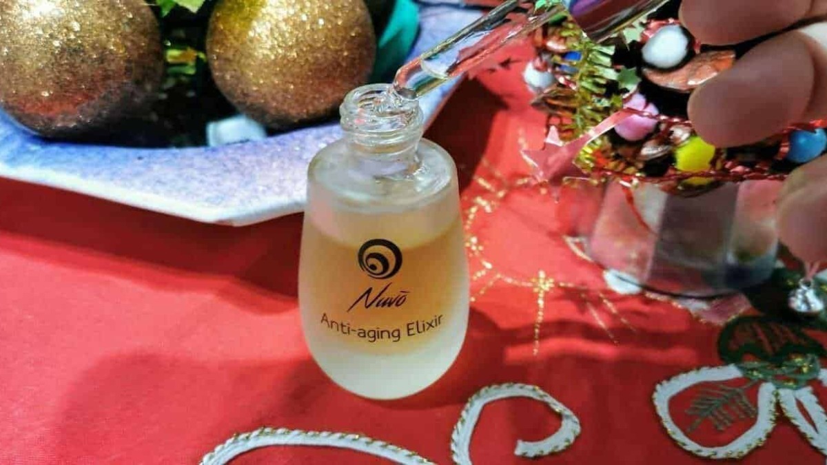 Anti-aging elisir in bottiglia con applicatore, cura della pelle e ringiovanimento, su tavolo rosso con decorazioni natalizie, prodotto di bellezza e benessere.