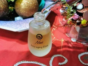 Anti-aging elisir in bottiglia con applicatore, cura della pelle e ringiovanimento, su tavolo rosso con decorazioni natalizie, prodotto di bellezza e benessere.
