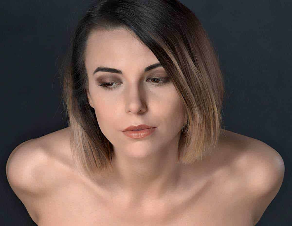 Bellissima donna giovane con trucco naturale, capelli castani corti, sguardo sereno e pelle luminosa, primo piano di bellezza femminile, modella con espressione irresistibile, ritratto di stile e eleganza femminile.
