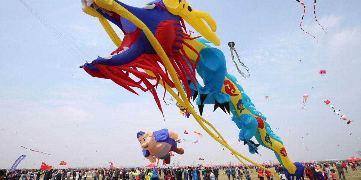 Colorati aquiloni a forma di dragone in cielo durante un festival, con una folla di persone che ammira lo spettacolo all'aperto. Atmosfera vivace e colorata, ideale per appassionati di eventi e cultura popolare.