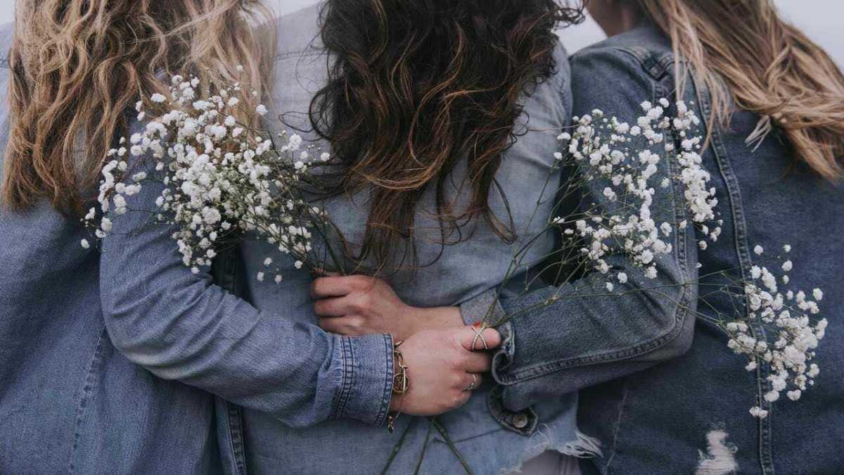 Fiore di gypsophila tra tre donne con denim, scatto ravvicinato durante il giorno, atmosfera spontanea e naturale, stile boho chic, simbolo di amicizia e moda casual.