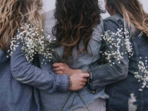 Fiore di gypsophila tra tre donne con denim, scatto ravvicinato durante il giorno, atmosfera spontanea e naturale, stile boho chic, simbolo di amicizia e moda casual.