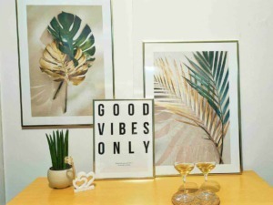 Fogli di monstera e palme in quadri decorativi con frasi motivazionali, pianta grassa e due calici di vino bianco su tavolo in stile boho chic, atmosfera rilassante e trendy per decorazioni d'interni.