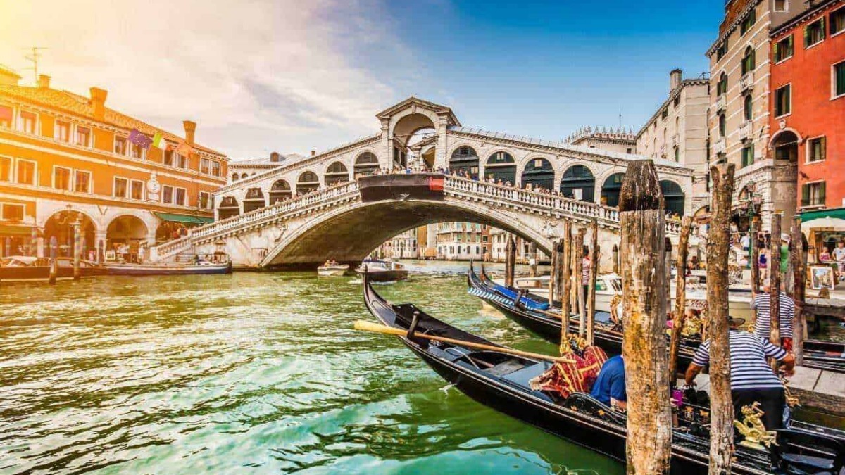 Venedig Ponte di Rialto con gondole e palazzi storici sotto cielo blu soleggiato, atmosfera romantica e turistica, immagini di viaggio e cultura veneziana, destinazione turistica ideale.