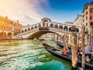 Venedig Ponte di Rialto con gondole e palazzi storici sotto cielo blu soleggiato, atmosfera romantica e turistica, immagini di viaggio e cultura veneziana, destinazione turistica ideale.