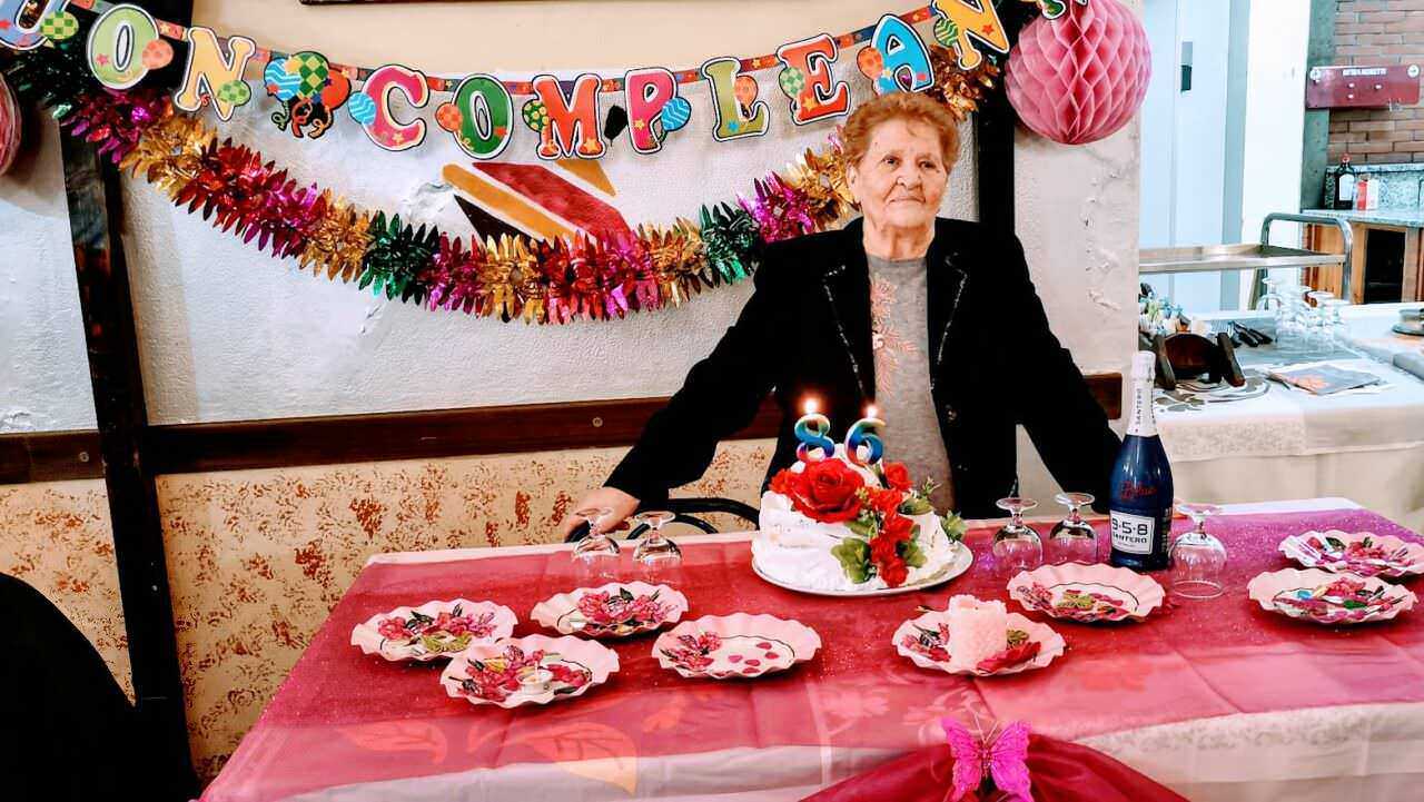 FOTO: Anziana donna sorridente con torta di compleanno decorata con rose rosse, allegria e festa, decorazioni di compleanno colorate, brindisi con spumante, buon intrattenimento in famiglia.