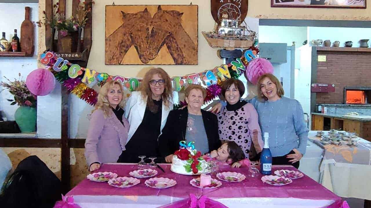 Festeggiamento di compleanno con famiglia e amici in un ristorante, decorazioni colorate, torta e brindisi in un'atmosfera calda e conviviale.