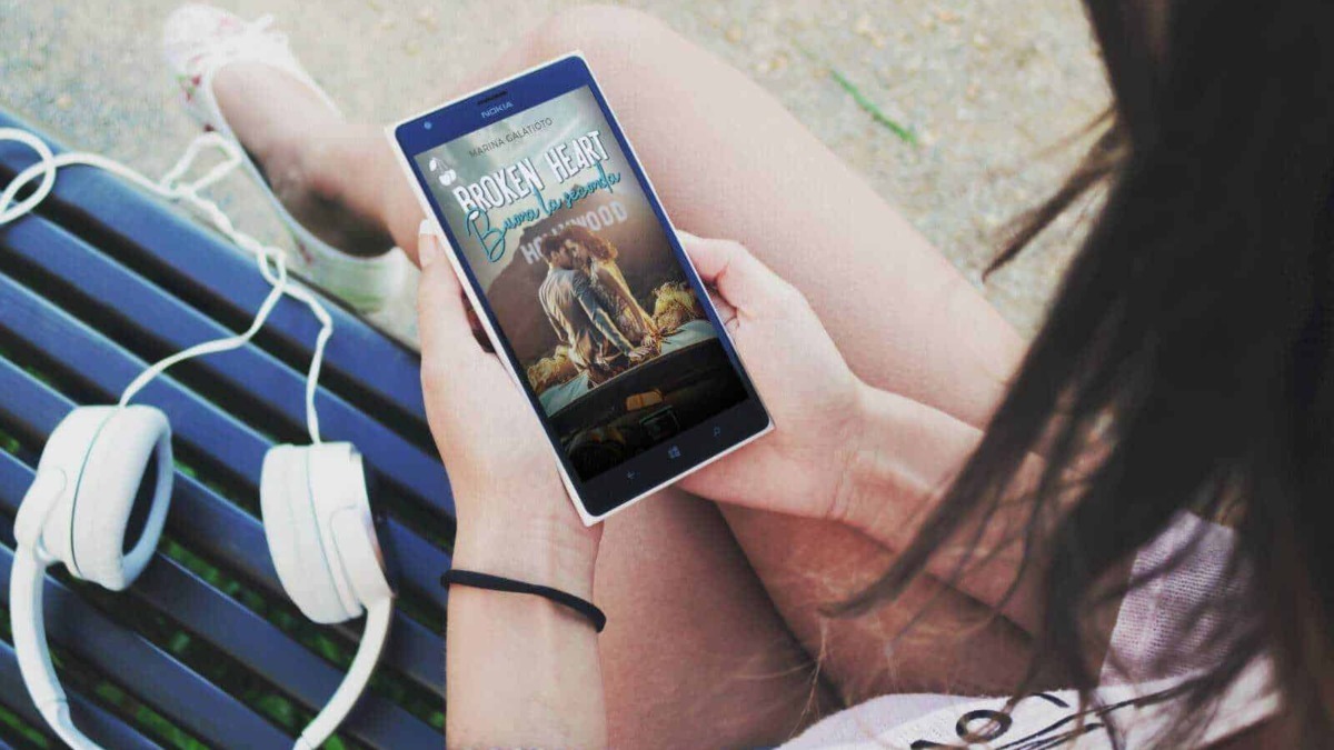 Scarpe e cuffie bianche, donna che guarda un ebook sullo smartphone mentre è seduta su una panchina all'aperto, ambientazione estiva, relax e tempo libero, tema lettura digitale e tecnologia.