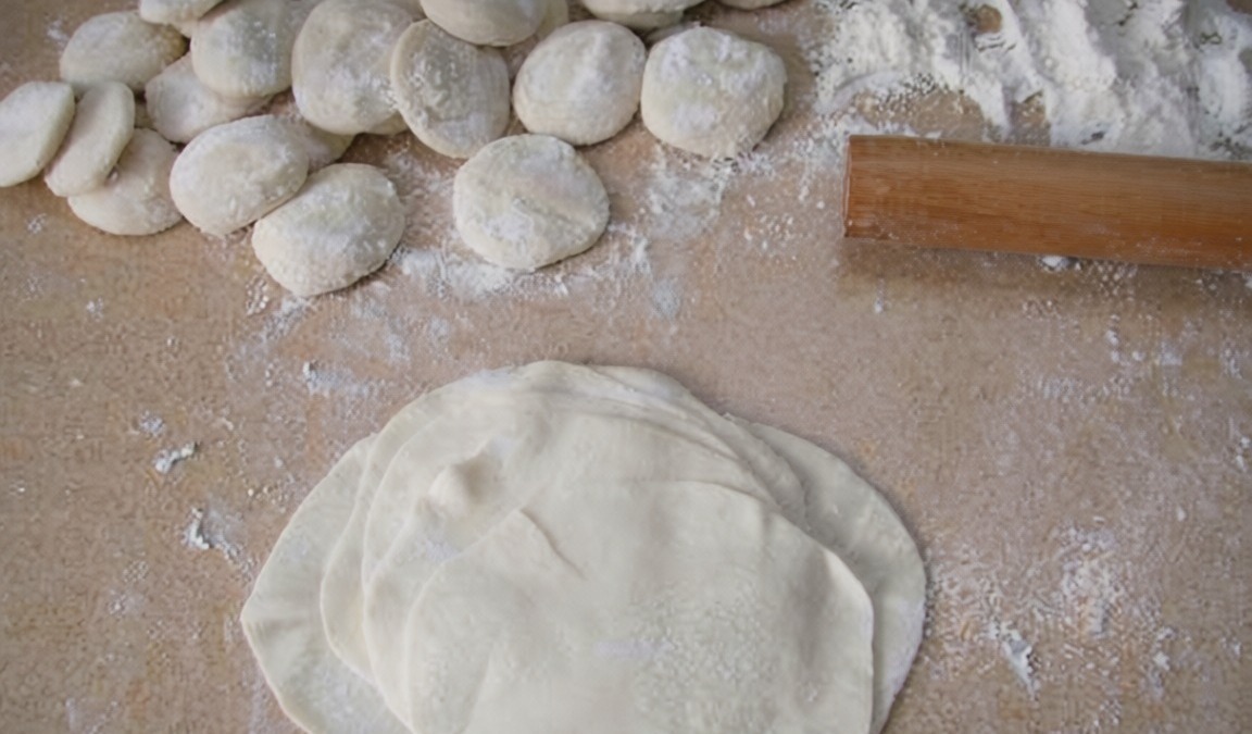 Tridioni di pasta fresca con farinata, palline di impasto e matterello su superficie infarinata, pronti per essere stesi.