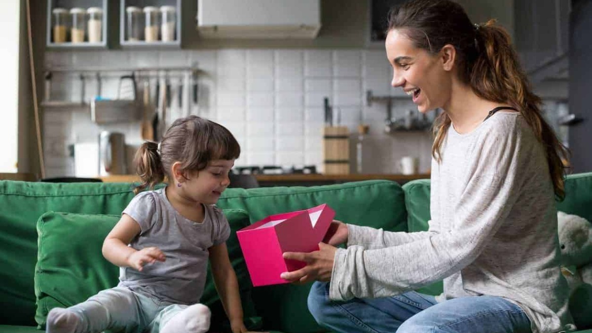 Regalo per bambina, mamma e figlia sorridenti che scartano un regalo in casa, atmosfera felice e affettuosa, momento speciale in famiglia, regali personalizzati.
