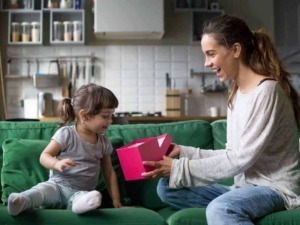 Regalo per bambina, mamma e figlia sorridenti che scartano un regalo in casa, atmosfera felice e affettuosa, momento speciale in famiglia, regali personalizzati.