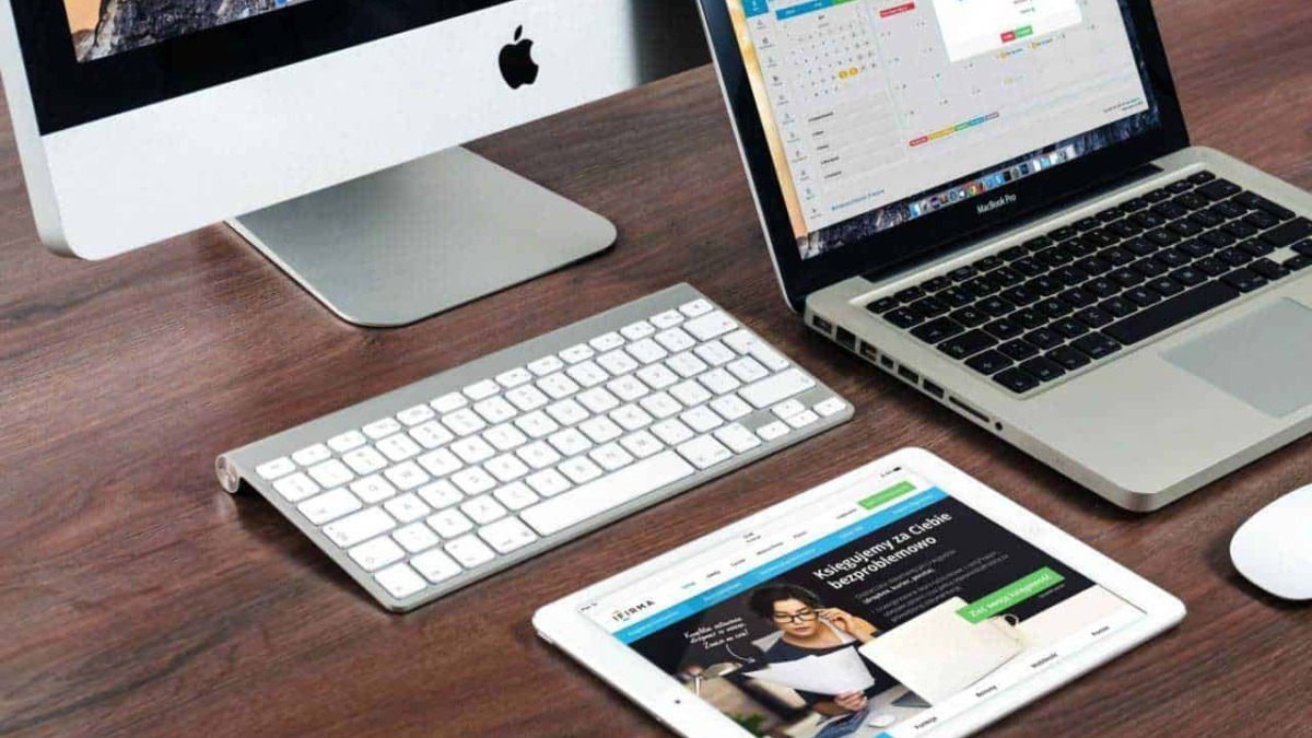Personal computer all-in-one iMac, MacBook e tablet con agenda digitale, strumenti per l'organizzazione e il lavoro smart, su scrivania in legno.