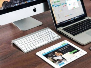 Personal computer all-in-one iMac, MacBook e tablet con agenda digitale, strumenti per l'organizzazione e il lavoro smart, su scrivania in legno.
