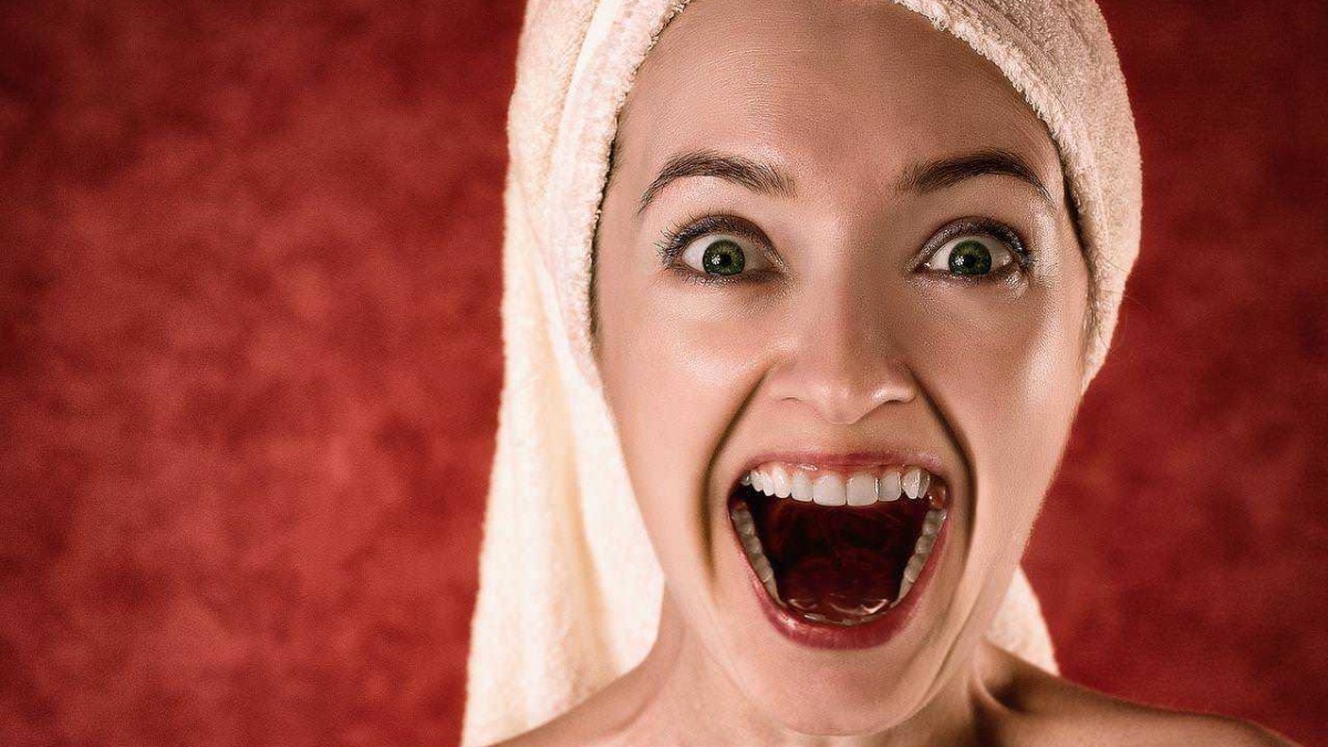 Femminina con asciugamano sul capo, espressione sorpresa e sorriso aperto, sfondo rosso, immagine di bellezza e benessere femminile, perfetta per articoli sulla cura della pelle e bellezza.