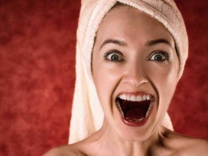 Femminina con asciugamano sul capo, espressione sorpresa e sorriso aperto, sfondo rosso, immagine di bellezza e benessere femminile, perfetta per articoli sulla cura della pelle e bellezza.