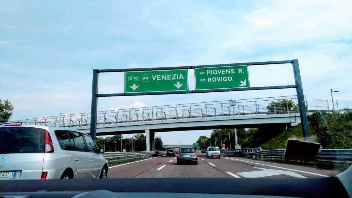 Vignetta autostradale con indicazioni per Venezia e Rovigo, vista dall'interno di un'auto lungo l'autostrada italiana in viaggio verso destinazioni turistiche e culturali.