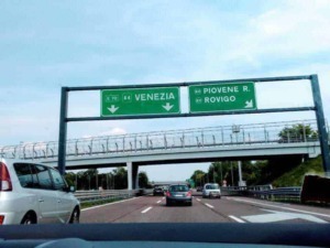 Vignetta autostradale con indicazioni per Venezia e Rovigo, vista dall'interno di un'auto lungo l'autostrada italiana in viaggio verso destinazioni turistiche e culturali.
