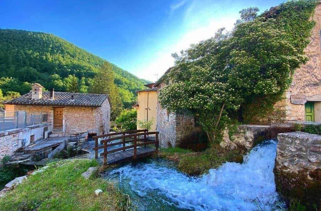 Prezzo di una pittoresca scena di un villaggio di montagna italiano con case di pietra e un torrente che scorre, immersa nella natura e nel verde, ideale per blog di viaggi e turismo rurale.
