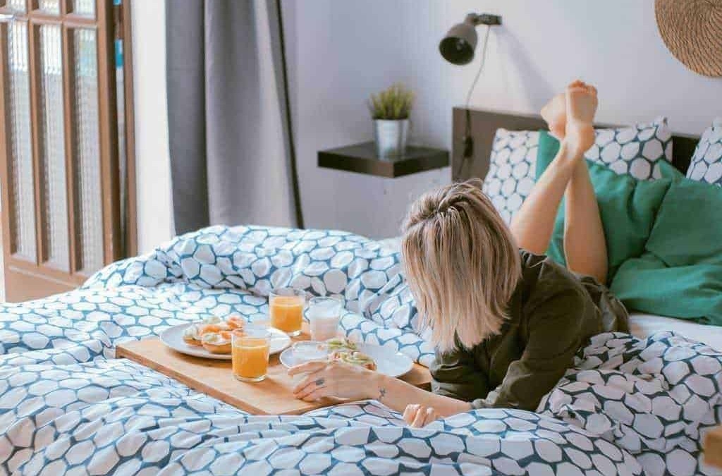 Colazione a letto con caffè e toast in camera da letto moderna, atmosfera accogliente, luce naturale, tessuti a motivi geometrici, stile di vita rilassante, comfort domestico.