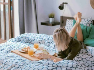 Colazione a letto con caffè e toast in camera da letto moderna, atmosfera accogliente, luce naturale, tessuti a motivi geometrici, stile di vita rilassante, comfort domestico.