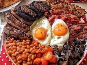 Frittata con uova, salsicce, hamburger, pomodorini e funghi su piatto di colazione italiana, colazione tradizionale con ingredienti ricchi e saporiti, immagine di un brunch sostanzioso e gustoso.