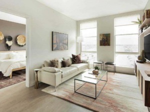 Luminoso soggiorno con grandi finestre, divano beige con cuscini decorativi, tavolino in vetro e scaffale con decorazioni in stile moderno, ideale per ambienti di casa accoglienti e di tendenza.