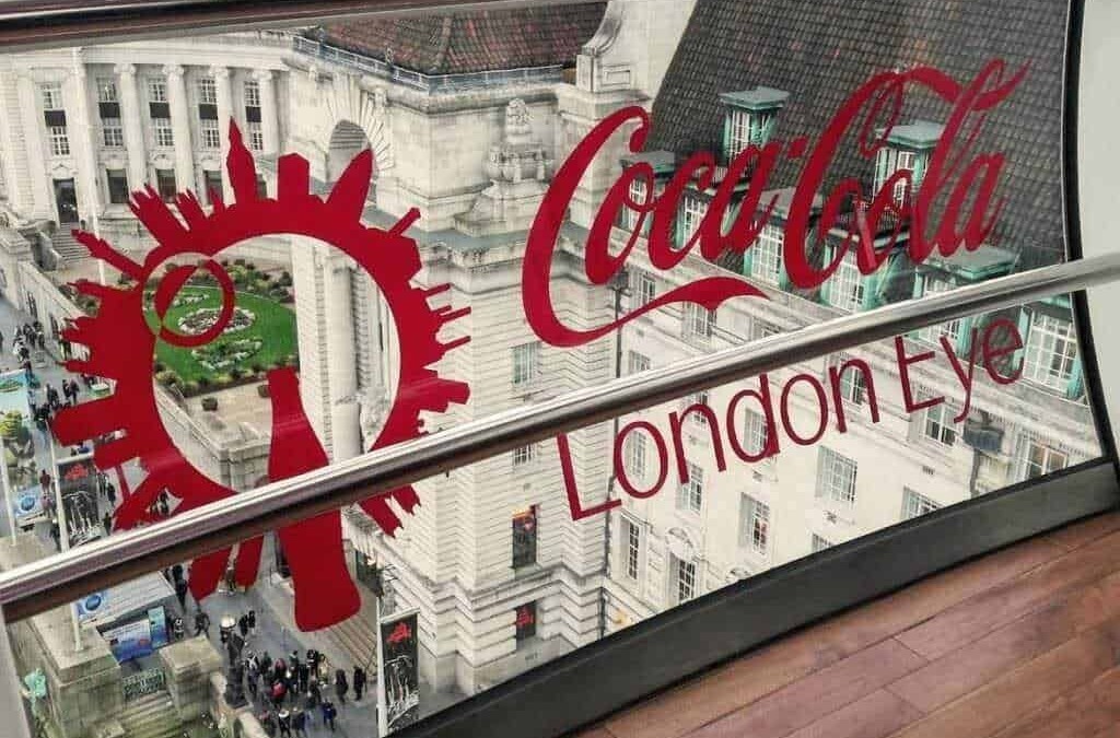 Vetro con logo Coca-Cola London Eye vista dall'alto su strada affollata a Londra, con edificio storico sullo sfondo, atmosfera urbana vivace e iconica attrazione turistica.