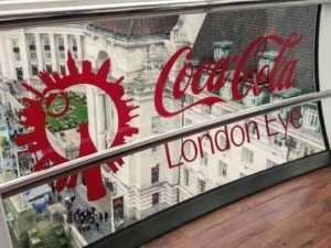 Vetro con logo Coca-Cola London Eye vista dall'alto su strada affollata a Londra, con edificio storico sullo sfondo, atmosfera urbana vivace e iconica attrazione turistica.