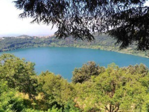 Lago circondato da alberi verdi, vista panoramica da un punto elevato con natura rigogliosa e cielo limpido.