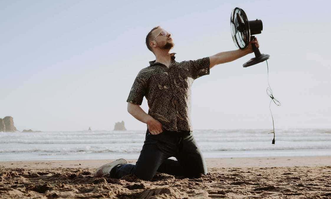 Fan da spiaggia con uomo che tiene in mano un ventilatore portatile, quindi foto di relax e comfort estivi, ambientazione naturale mare, resistenza al caldo