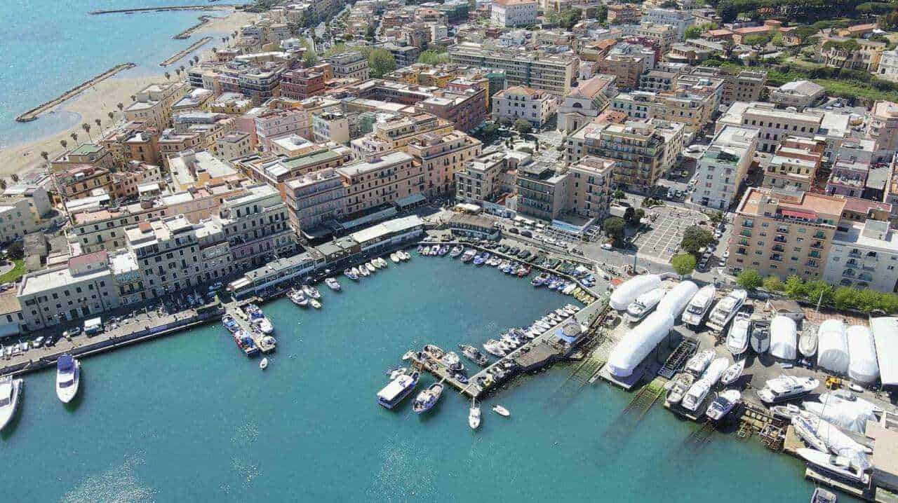 Vita di mare e città costiera, porto turistico con yacht e imbarcazioni, veduta aerea del centro storico di una località marina in Italia, con edifici colorati e mare cristallino.