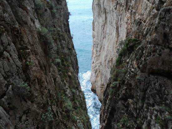 Scogliera calcarea con stretto tra le rocce che si apre sul mare, paesaggio naturale mozzafiato in Italia.