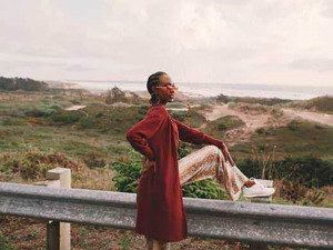 Unisex fashion outdoor, donna seduta sul parapetto con paesaggio naturale, moda casual, look elegante, stile di vita all'aperto, outfit autunnale, casual chic, moda sostenibile.