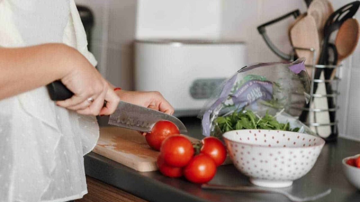Pomodori freschi tagliati mentre si cucina in cucina, alimenti sani e genuini, preparazione di una fresca insalata o piatto mediterraneo.