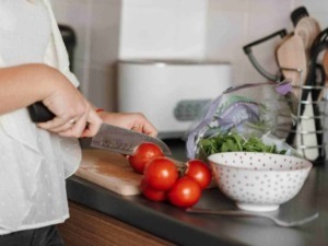 Pomodori freschi tagliati mentre si cucina in cucina, alimenti sani e genuini, preparazione di una fresca insalata o piatto mediterraneo.