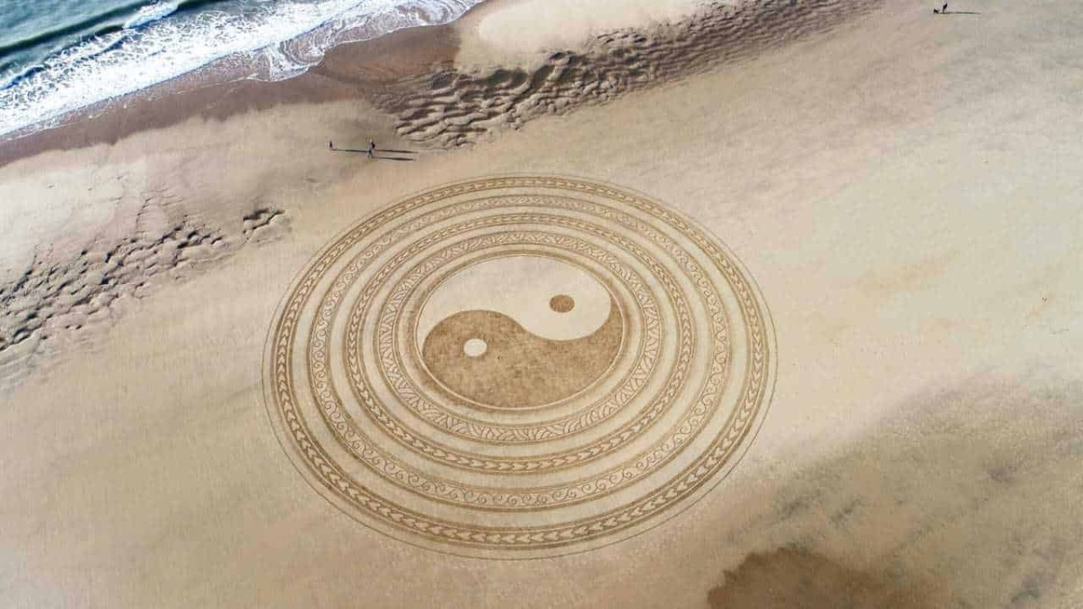 Yin Yang disegnato sulla spiaggia con motivi mistici e simbolismo spirituale, che si affaccia sul mare e sulla sabbia.