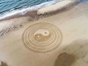 Yin Yang disegnato sulla spiaggia con motivi mistici e simbolismo spirituale, che si affaccia sul mare e sulla sabbia.