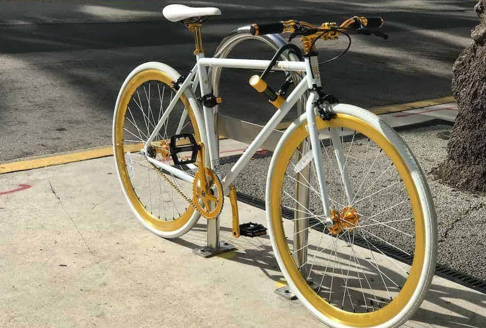 Originale bicicletta decorata con dettagli bianchi e gialli, posta sul marciapiede di fronte a una strada asfaltata, perfetta per appassionati di ciclismo e outdoor.