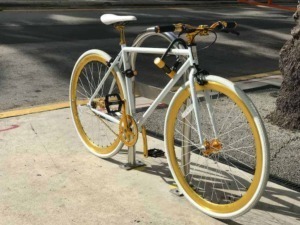 Originale bicicletta decorata con dettagli bianchi e gialli, posta sul marciapiede di fronte a una strada asfaltata, perfetta per appassionati di ciclismo e outdoor.